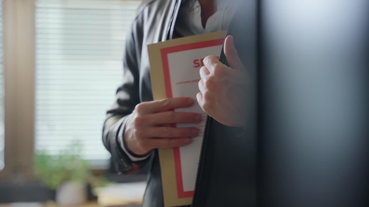 Man stealing and hiding top secret file folder in leather jacket inside office. Mysterious government agent or spy holding envelope with classified documents and information. Taking confidential file