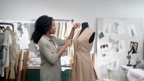 young woman, clothing designer making measurements with a measuring tape of the new dress and smiling at camera in studio