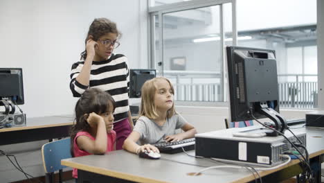 chica rubia sentada y escribiendo con confianza en el teclado mientras dos compañeros de clase miran