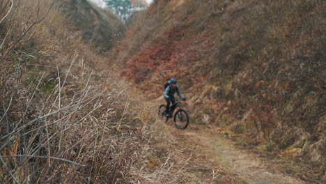 ciclista masculino con mochila montando una bicicleta de montaña en la colina por el camino en medio del valle