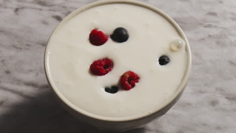 granola cereals falling into white bowl filled with yogurt on the background