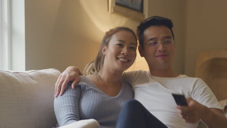 loving asian couple relaxing on sofa at home watch tv in evening together