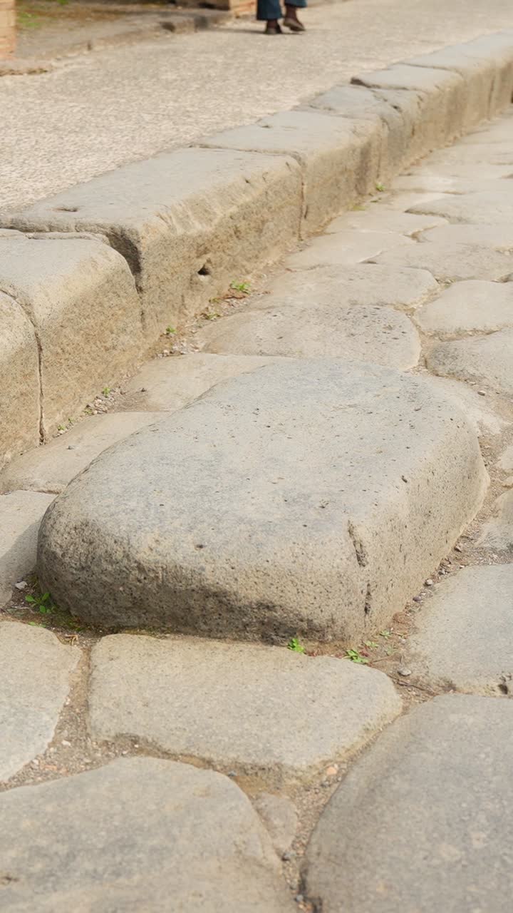 Vertical close-up of a large stepping stone on a Pompeii street, with worn Roman paving and raised curb revealing ancient pedestrian road design in Italy