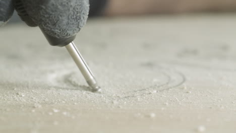 woodworker using electric engraving tool to make carved decoration on piece of wood, close-up