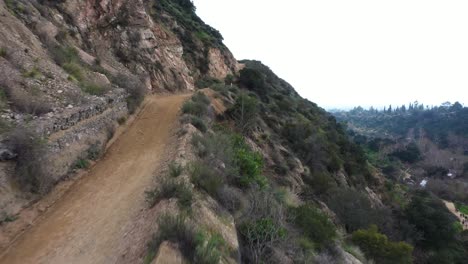 Aerial-push-in-landscape-shot-beside-a-trail-road-with-hikers-on-a-cliff-in-the-National-Forest-in-Pasadena,-California