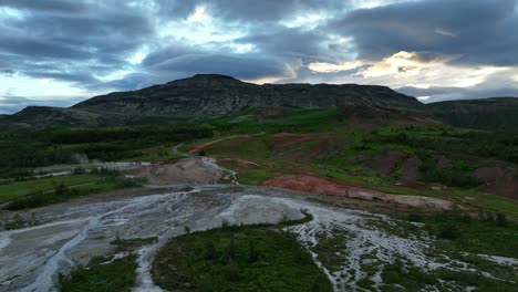 vista aérea de la zona geotérmica de geysir en islandia, que muestra el terreno humeante, las vibrantes colinas rojas y un sorprendente telón de fondo montañoso al atardecer.