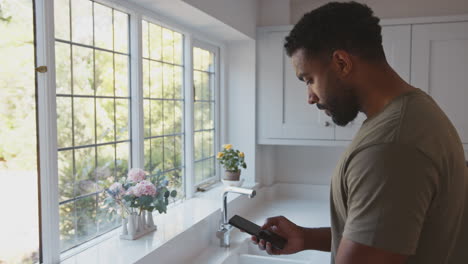 Cerca-De-Un-Soldado-Americano-En-Uniforme-En-La-Cocina-De-Vacaciones-En-Casa-Con-Teléfono-Móvil