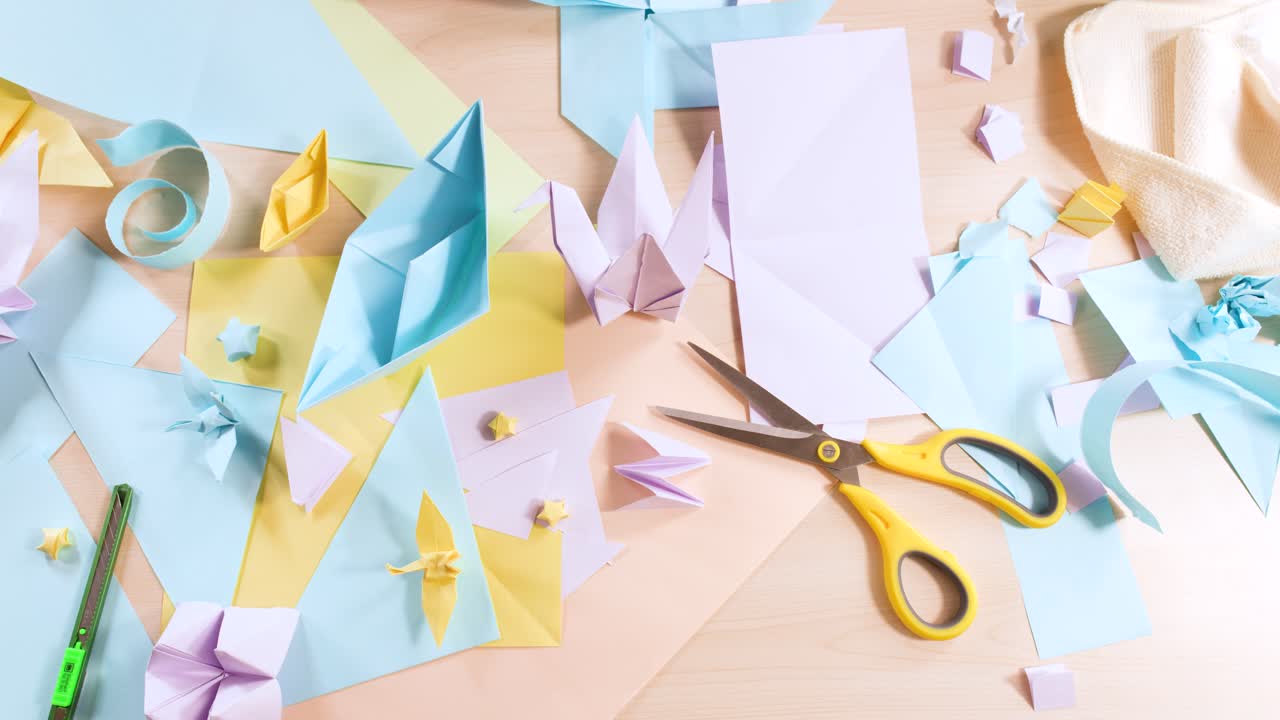 Un'inquadratura dall'alto cattura diverse forme di origami color pastello e strumenti per il crafting su una scrivania