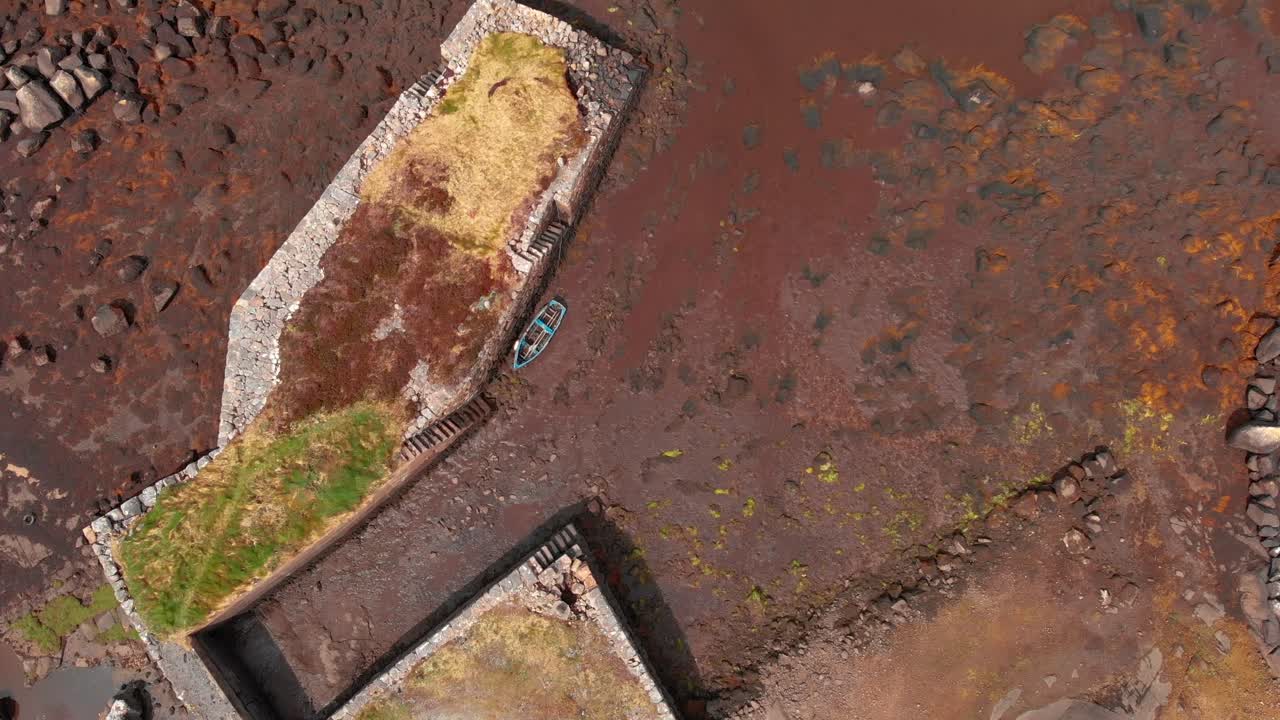 Rekaman drone dari atas sebuah dermaga batu bersejarah dan perahu dayung kecil saat air surut di Connemara, Irlandia. Ideal untuk film dokumenter perjalanan dan konten warisan regional.