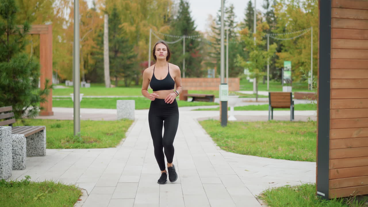 Front view of sporty woman running in decorated park during autumn. Ideal for fitness, outdoor jogging, and healthy lifestyle content with natural green park background