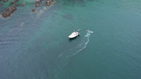 Amplia-Vista-Aérea-Orbitando-Una-Moto-De-Agua-Y-Un-Bote-Pequeño-Frente-A-La-Costa-De-Cornualles-En-El-Reino-Unido