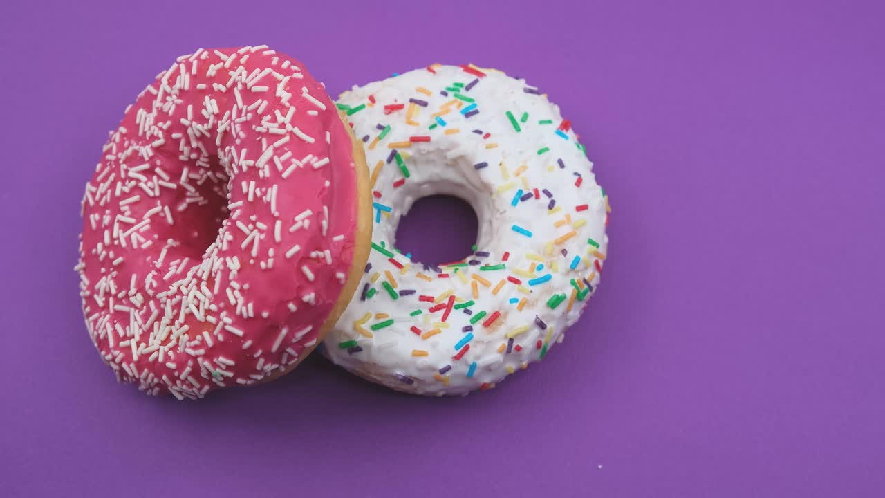 girando un primer plano de rosas y blancas sabrosas y deliciosas rosquillas dulces con salpicaduras coloridas sobre un fondo púrpura.