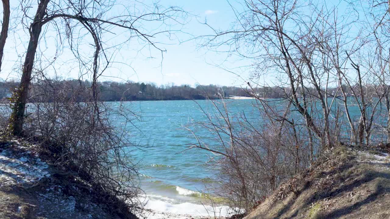 A peaceful winter scene at Lake Ronkonkoma, Long Island. Clear blue skies reflect over shimmering icy waters, creating a tranquil moment of natural beauty. Captures the serene charm of the season.
