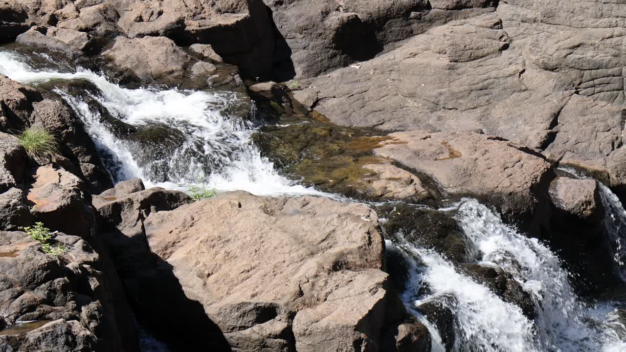 El agua fluye dinámicamente sobre afloramientos rocosos iluminados por el sol