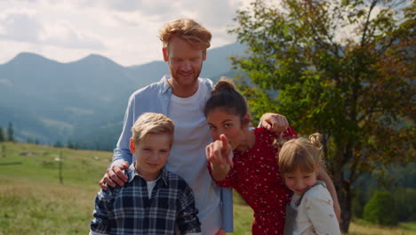 smiling family posing mountains close up. parents kids waving hands on nature.