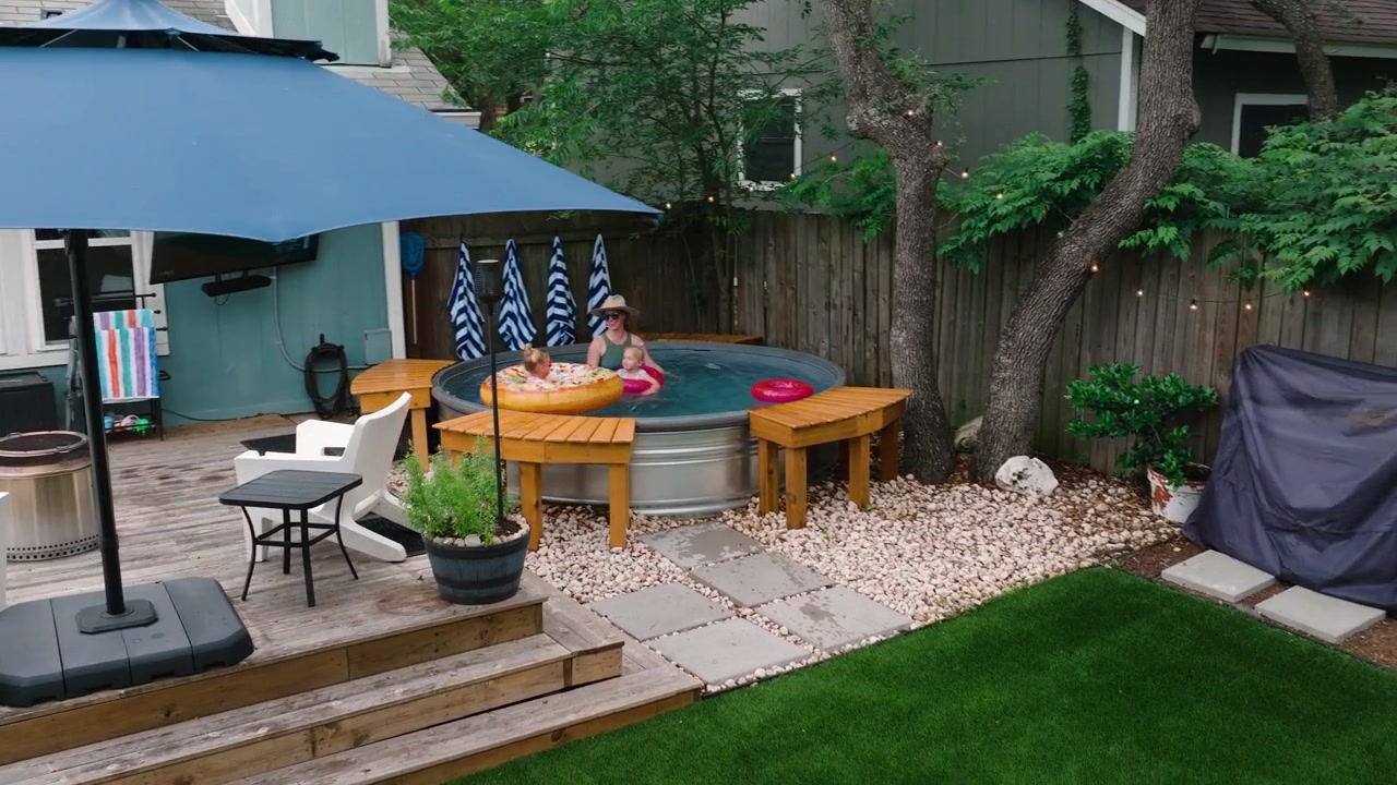 family playing in backyard pool deck umbrella, turf yard, Luxury outdoor living ads, summer lifestyle, and home property content aerial wide drone shot 4k