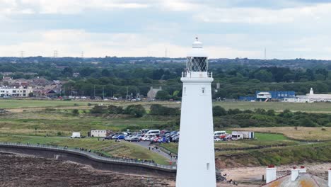 drone camera smoothly pans across st. mary’s lighthouse, revealing surrounding rocky shoreline, grassy fields, and distant town under soft daylight with overcast skies