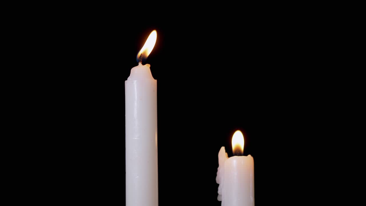 Due candele di paraffina bianche bruciano con fiamma gialla, su sfondo nero. 4K