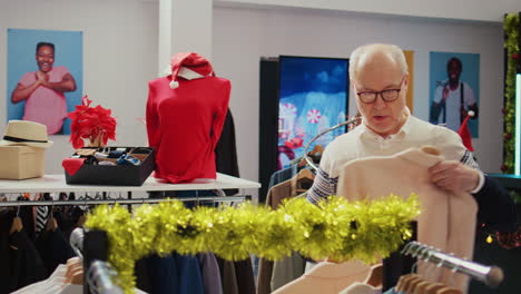 octogenarian man in xmas decorated shopping mall store trying to determine if elegant blazer is the right fit. old shopper in christmas adorn fashion boutique during winter holiday season