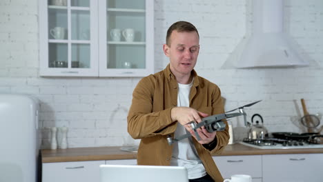 smiling man with a drone in flat. young man holding a drone and a cup in the kitchen. funny man with a drone indoors.