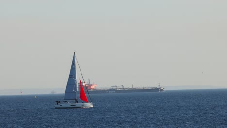 sailboat passing by a distant cargo ship