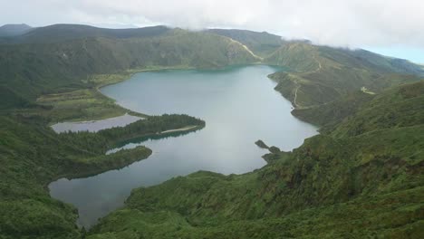 Beautiful-aerial-view-of-Lagoa-do-Fogo-surrounded-by-lush-green-hills-and-a-cloudy-sky