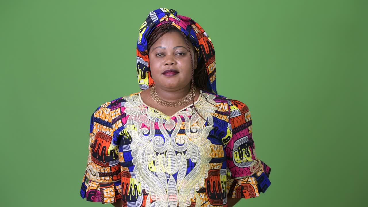 Overweight beautiful African woman wearing traditional clothing against green background