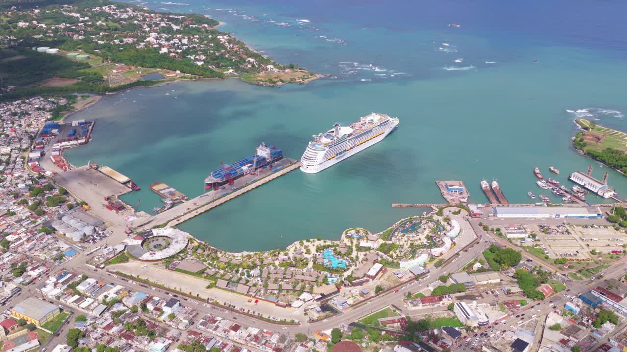 Dronevisning af Taino Bay krydstogthavn i Puerto Plata, Den Dominikanske Republik, med et stort krydstogtskib lagt til kaj i turkisblåt caribisk vand nær en tropisk kystby. Ovenfra.