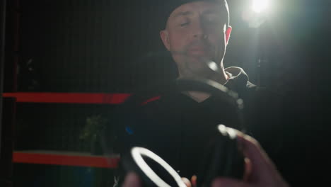 a cheerful man in black clothes holds a pair of headphones, smiling warmly in a dark studio room, accentuated by a subtle backlight creating a soft glow that highlights his joyful expression