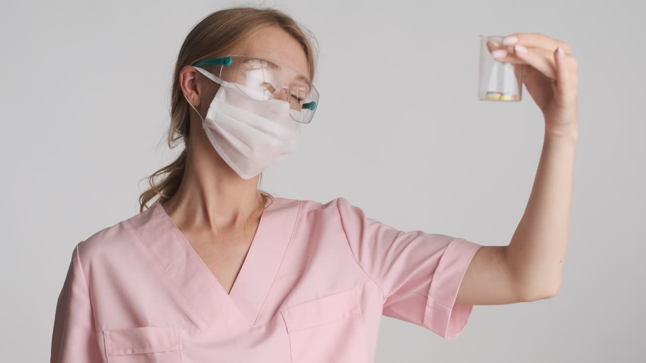 doctora caucásica con gafas de seguridad y máscara sosteniendo un frasco con pastillas.