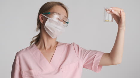 Caucasian-female-doctor-in-safety-goggles-and-mask-holding-flask-with-pills.