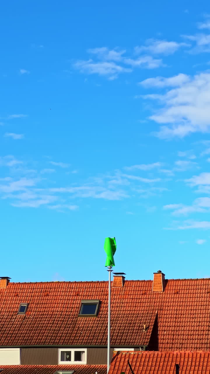 Un vestito verde brillante sventola in cima a un'alta asta su uno sfondo di cielo azzurro limpido e tetti di tegole rosse in un quartiere tranquillo.