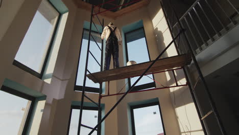 wide low angle shot: a builder in overalls primes the wall in the house. stands on high scaffolding