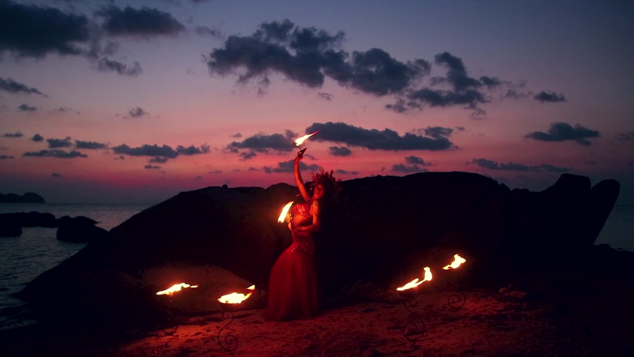 Beautiful, erotic and sensual belly dancer, performing with fire palm torch props, on the beach during golden hour.