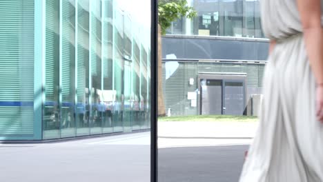 una mujer de negocios elegante lleva una bolsa y pasa por delante de un edificio de oficinas con fachada de cristal reflectante que va a trabajar en el distrito financiero