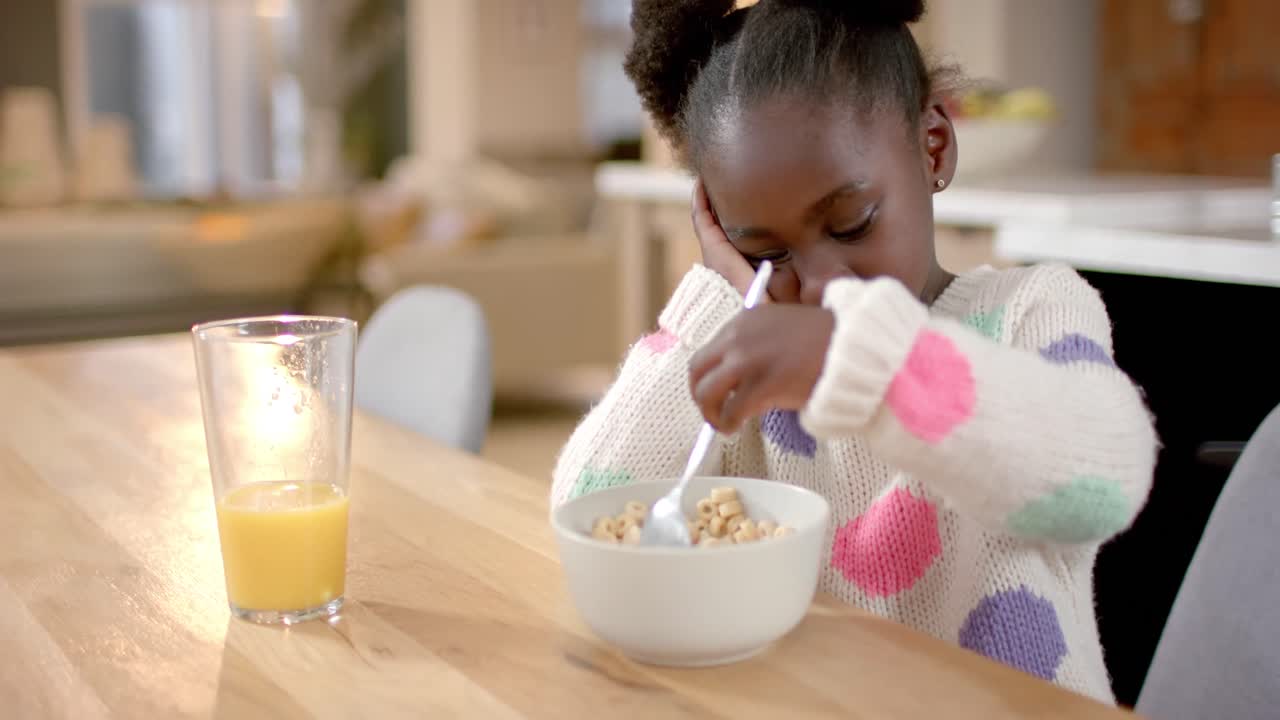 Fille afro-américaine mangeant des céréales avec du lait dans la cuisine, ralenti
