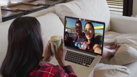 african american woman holding a coffee cup having a video call on laptop sitting on couch at home