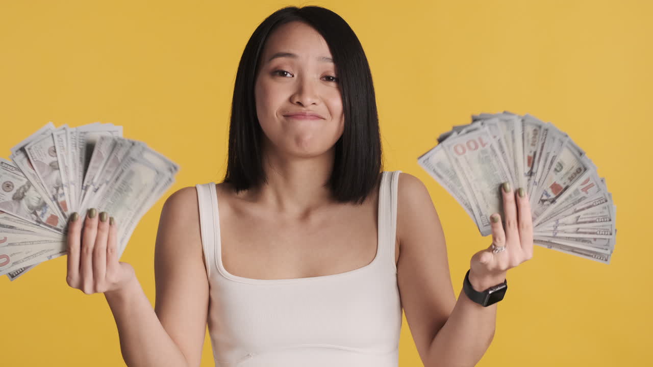 카메라 앞에서 돈을 들고 있는 아시아 여성이 행복해 보입니다.