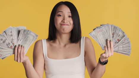 asian woman looking happy while holding money on camera.