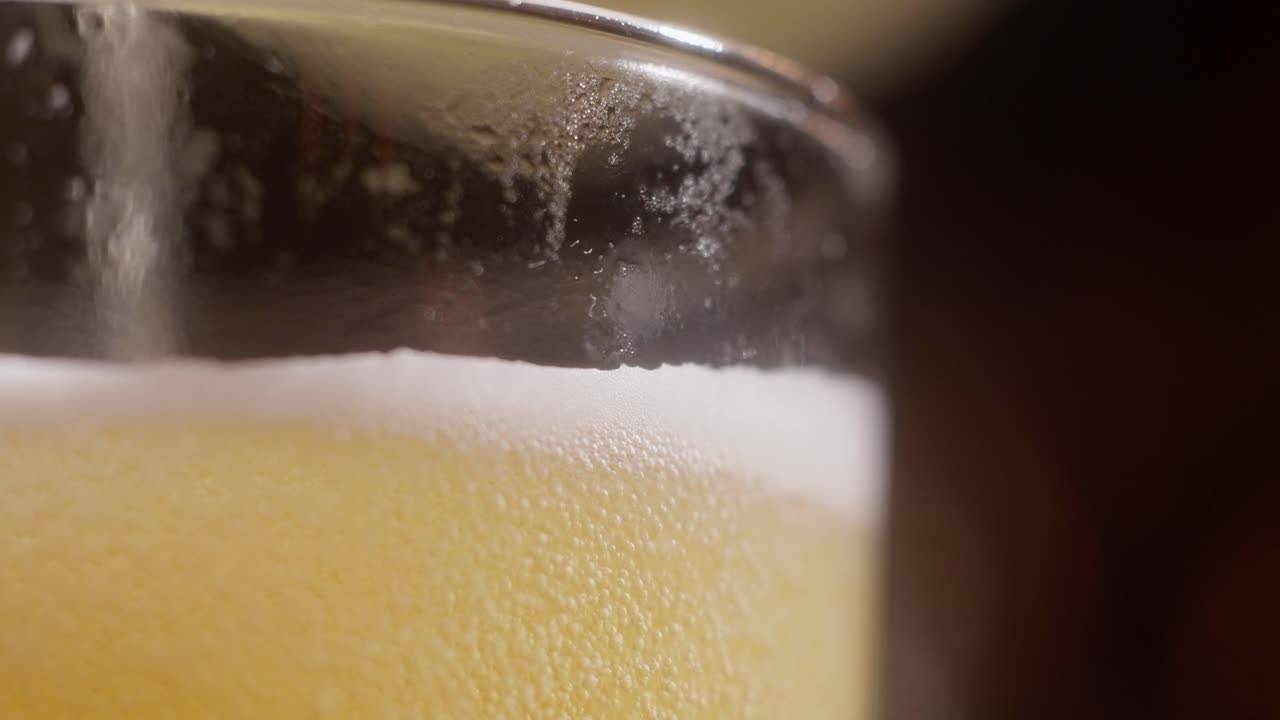 Golden beer pours smoothly into a glass, captured in a close-up shot with foamy detail