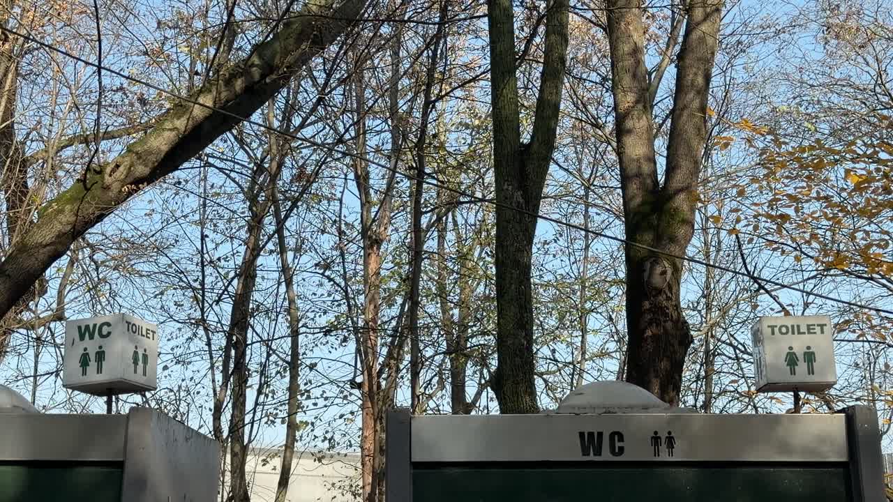 높은 가을 나무들로 둘러싸인 시설 위에 공용 화장실 표지판이 있어요