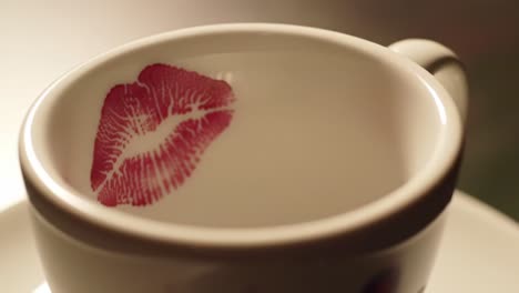 a close-up view of a coffee cup featuring a bright red lipstick print inside. the warm background suggests a cozy atmosphere, perfect for intimate gatherings or romantic moments.