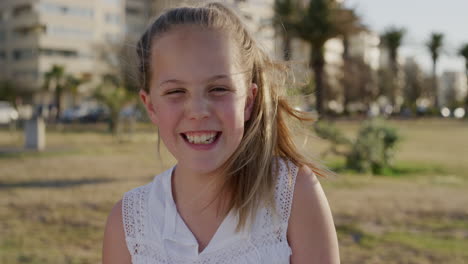 Retrato-Hermosa-Niña-Riendo-Feliz-Disfrutando-De-Un-Relajado-Día-De-Vacaciones-De-Verano-En-Un-Cálido-Atardecer-Parque-Urbano-Viento-Soplando-Cabello-Infancia-Juguetona