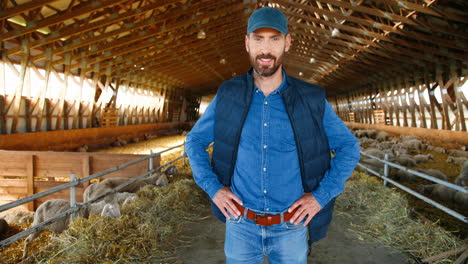 camera zooming on young caucasian man looking at camera in stable with sheep flock