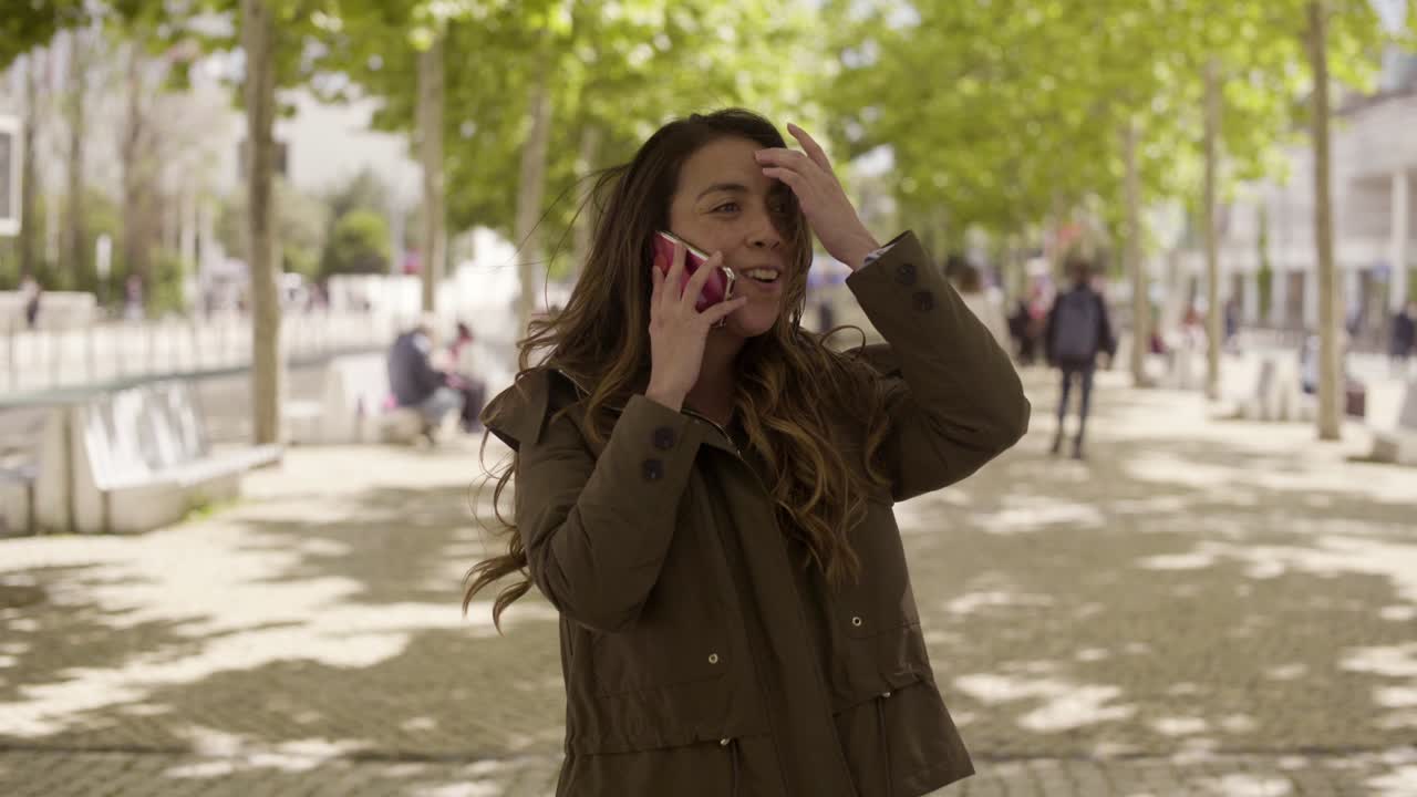 una joven sonriente llamando a un amigo mientras estaba de pie en una calle soleada.