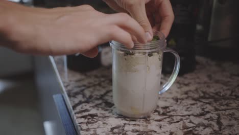 Hand-Of-A-Person-Adding-Some-Mint-Leaves-For-Banana-Smoothie
