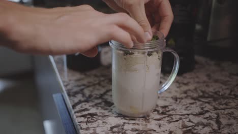 hand of a person adding some mint leaves for banana smoothie