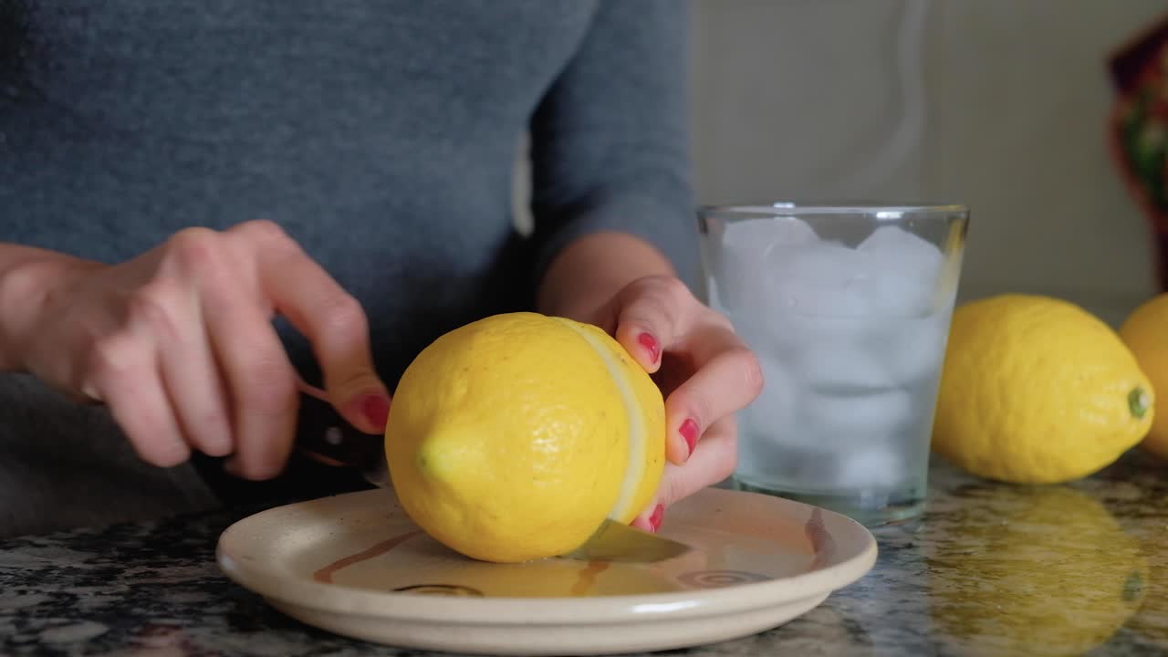 Mujer cortando un limón por la mitad con un cuchillo y vaso de limonada al lado