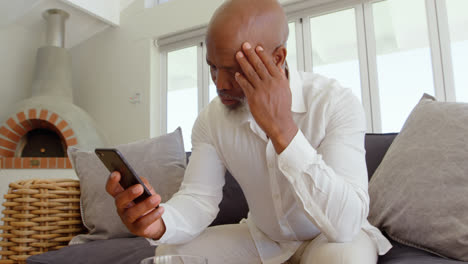 Front-view-of-mature-black-man-sitting-on-the-couch-and-using-mobile-phone-in-a-comfortable-home-4k