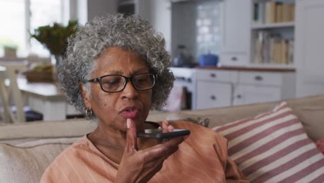 mujer afroamericana mayor hablando en un teléfono inteligente mientras estaba sentada en el sofá en casa